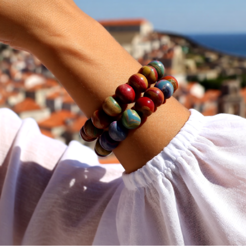 Colourful beaded bracelet on a wrist with a scenic background and 'Vacation Essential' text.