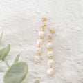 Pearl and gold drop earrings on a light background with greenery
