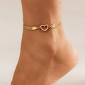 Gold anklet with a heart-shaped clasp on a foot against a neutral background