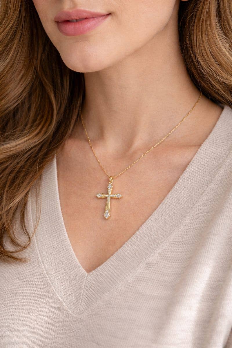 Gold cross necklace with small diamonds on a beige sweater