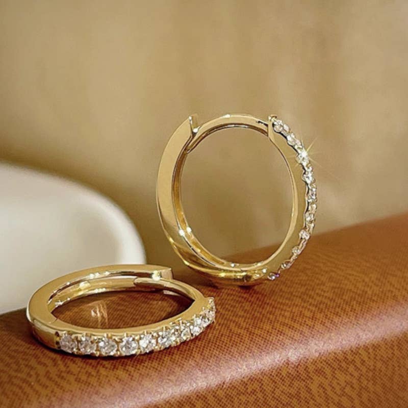 Gold hoop earrings with diamond accents on a brown surface.
