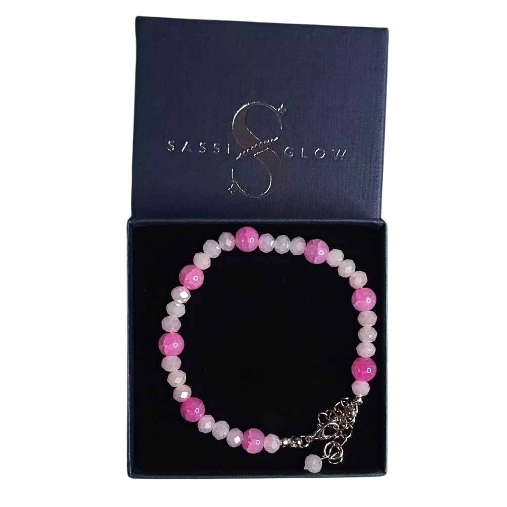 Pink and white beaded bracelet with silver charm in a gift box with 'Sassiglow' branding.
