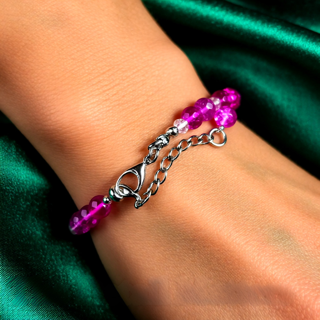 Bracelet with pink beads and silver chain on a wrist against a green fabric background