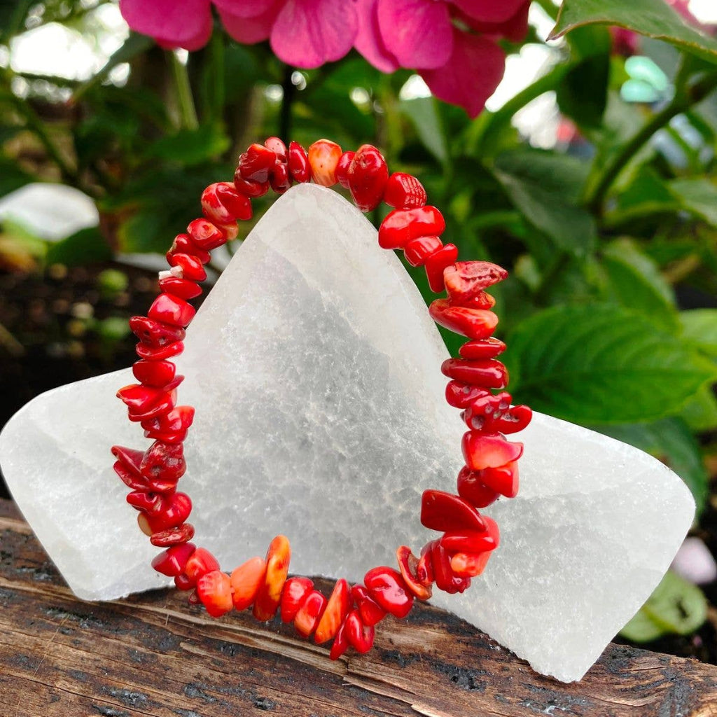 Red coral bracelet on a white stone with pink flowers in the background