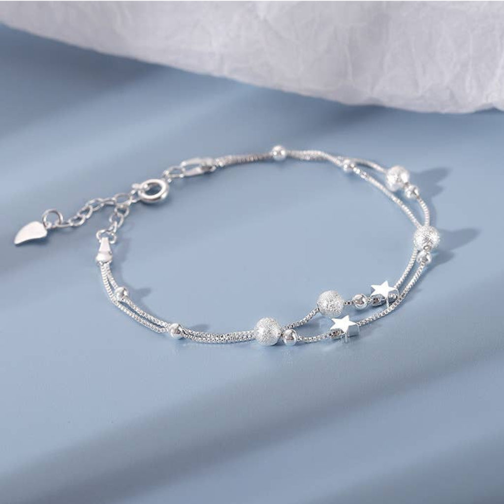 Silver bracelet with star and heart charms on a light blue background